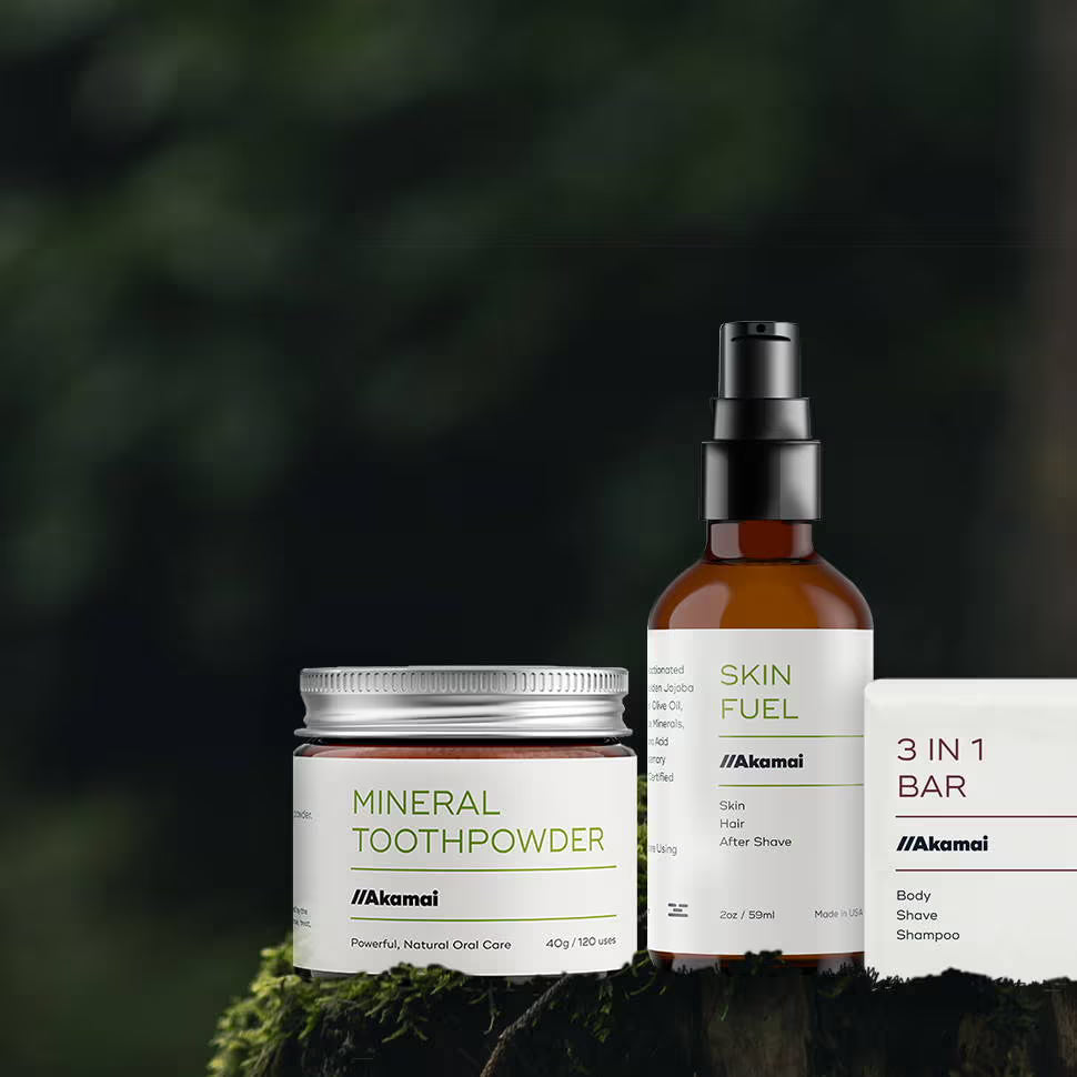 Akamai Basics natural oral and body care products: mineral toothpowder, skin fuel, and 3-in-1 bar on a rustic background.